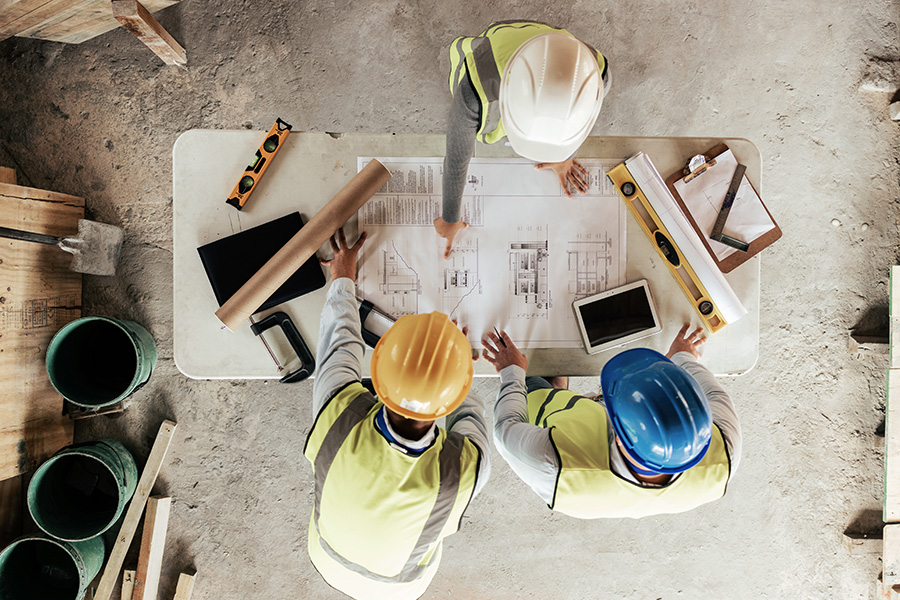 Image of a team engaged in project planning and analysis. The photo shows team members gathered around, possibly with plans or digital devices, actively discussing and strategizing, highlighting a collaborative and focused work environment.